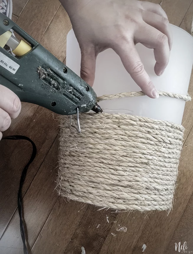 Holding a hot glue gun and gluing sisal rope on the trash can
