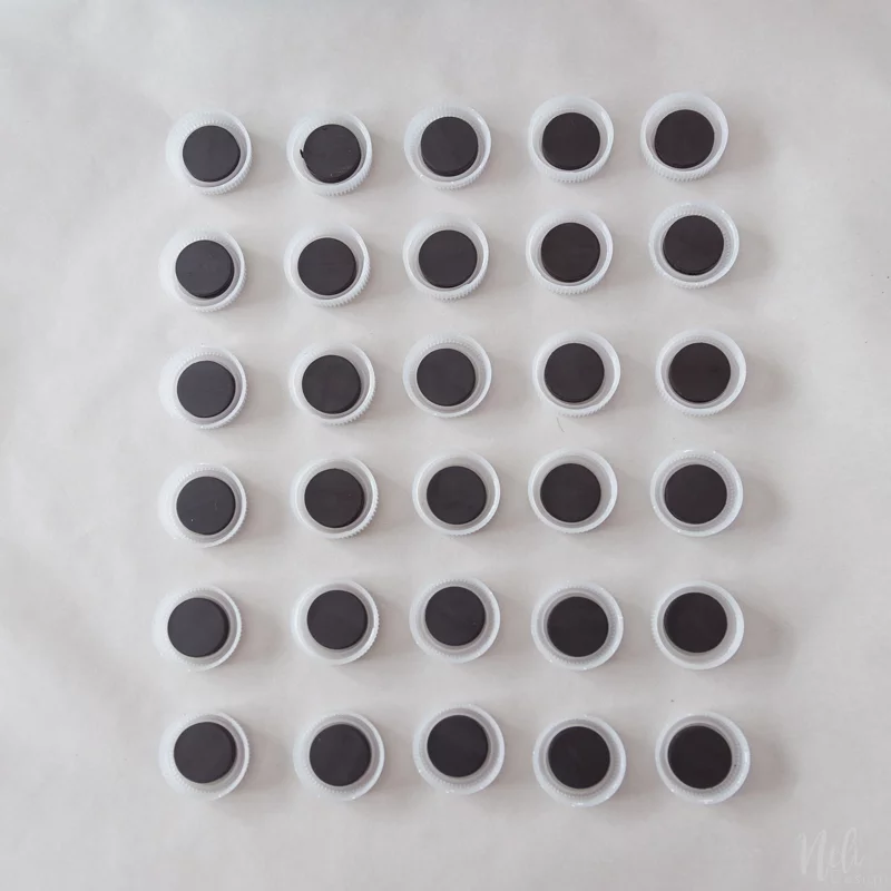 The bottle caps and magnets layout in a grid to make the magnetic gaming time chart