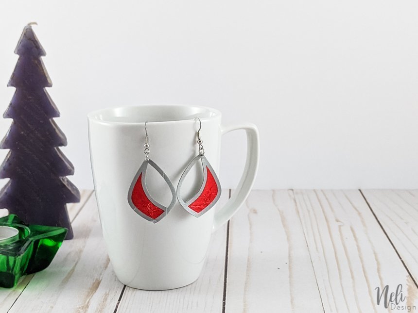 faux leather and red vinyl earrings hung on a mug with a fir tree and a star candle