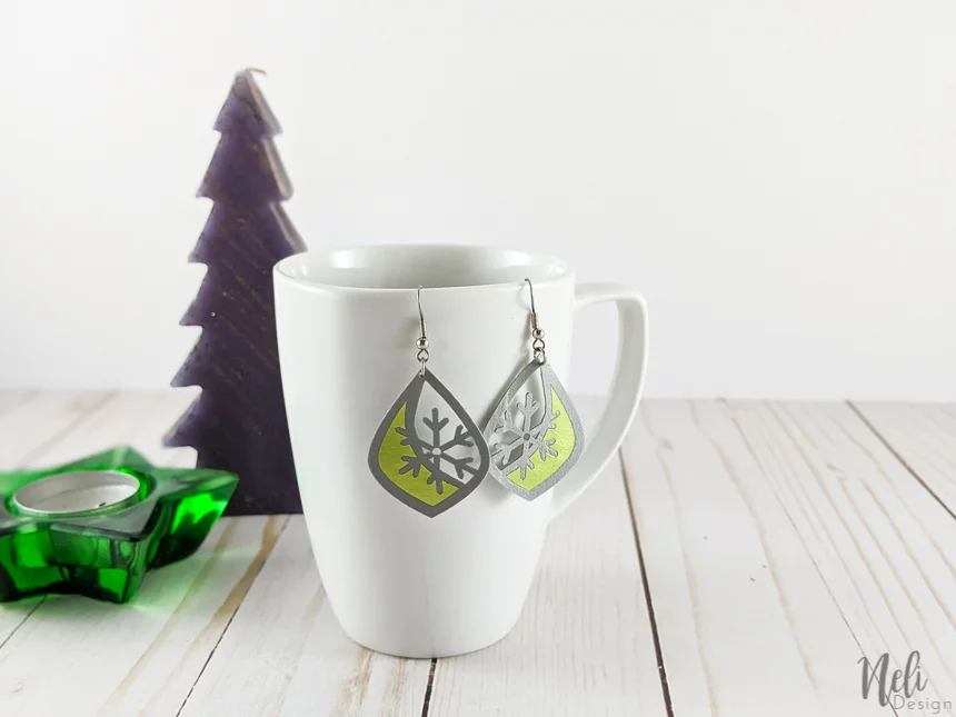 faux leather and green vinyl earrings hung on a mug with a fir tree and a star candle