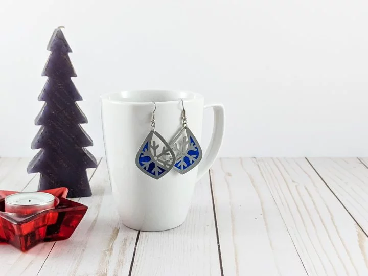 faux leather and blue vinyl earrings hung on a mug with a fir tree and a star candle