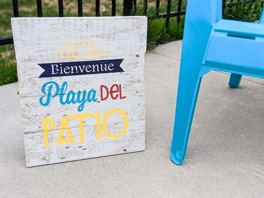 Painted Wood sign made with a Cricut Stencil saying Welcome Playa del patio next to a adirondack chair