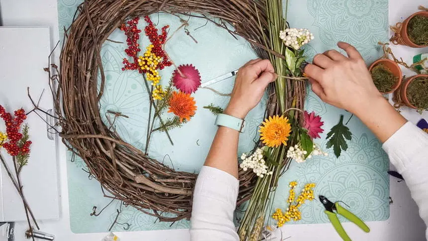 Using knots to attach the DIY chrysanthemum paper flowers to the grapevine wreath