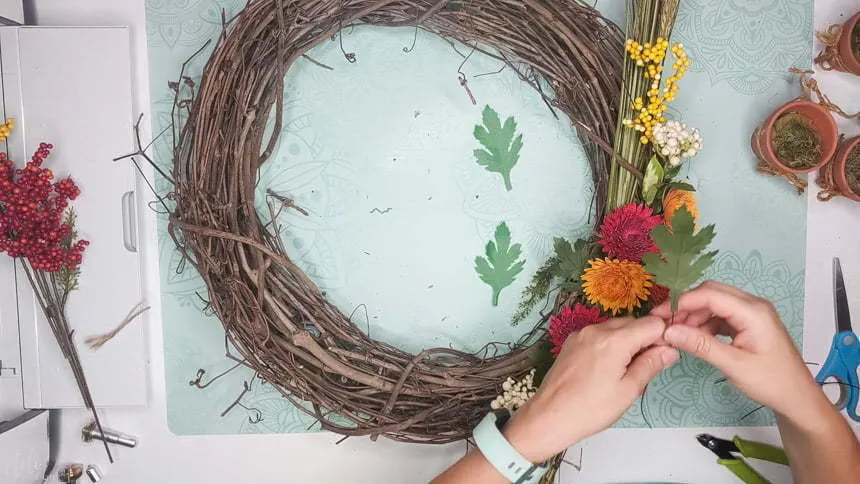Using wires to add the DIY chrysanthemum paper flowers leaves to the grapevine wreath